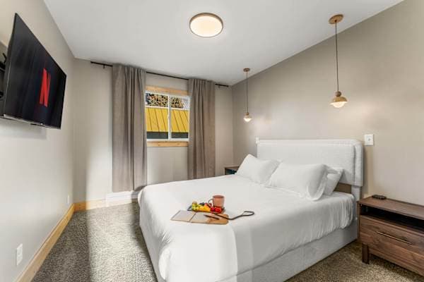 【Bedroom 2】 Queen bed, blackout curtains, pendant lighting — quiet side of the building.